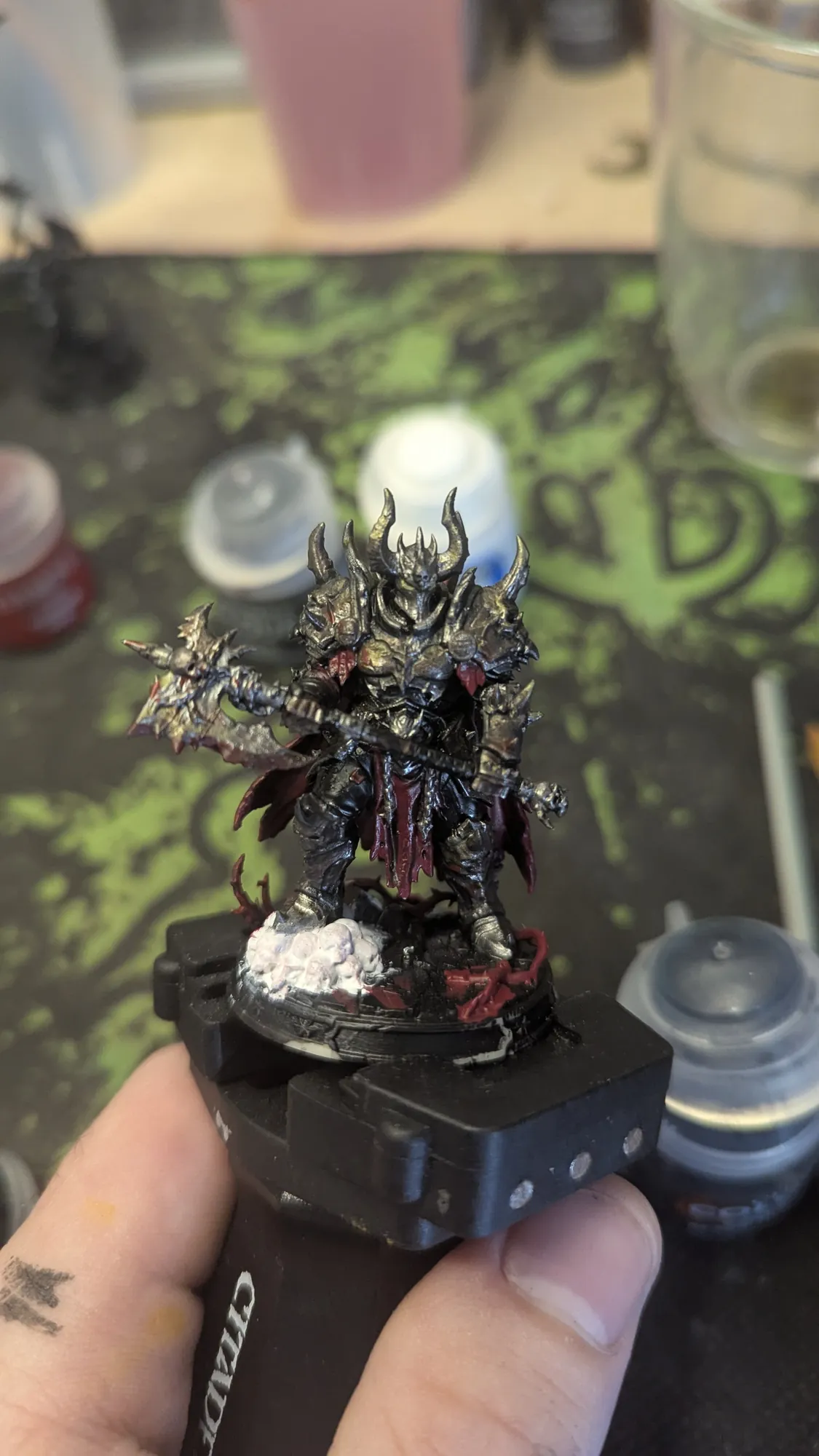 Figurine Demonlord Arkonath montée sur poignée de peinture, en cours de mise en couleur à l'établi