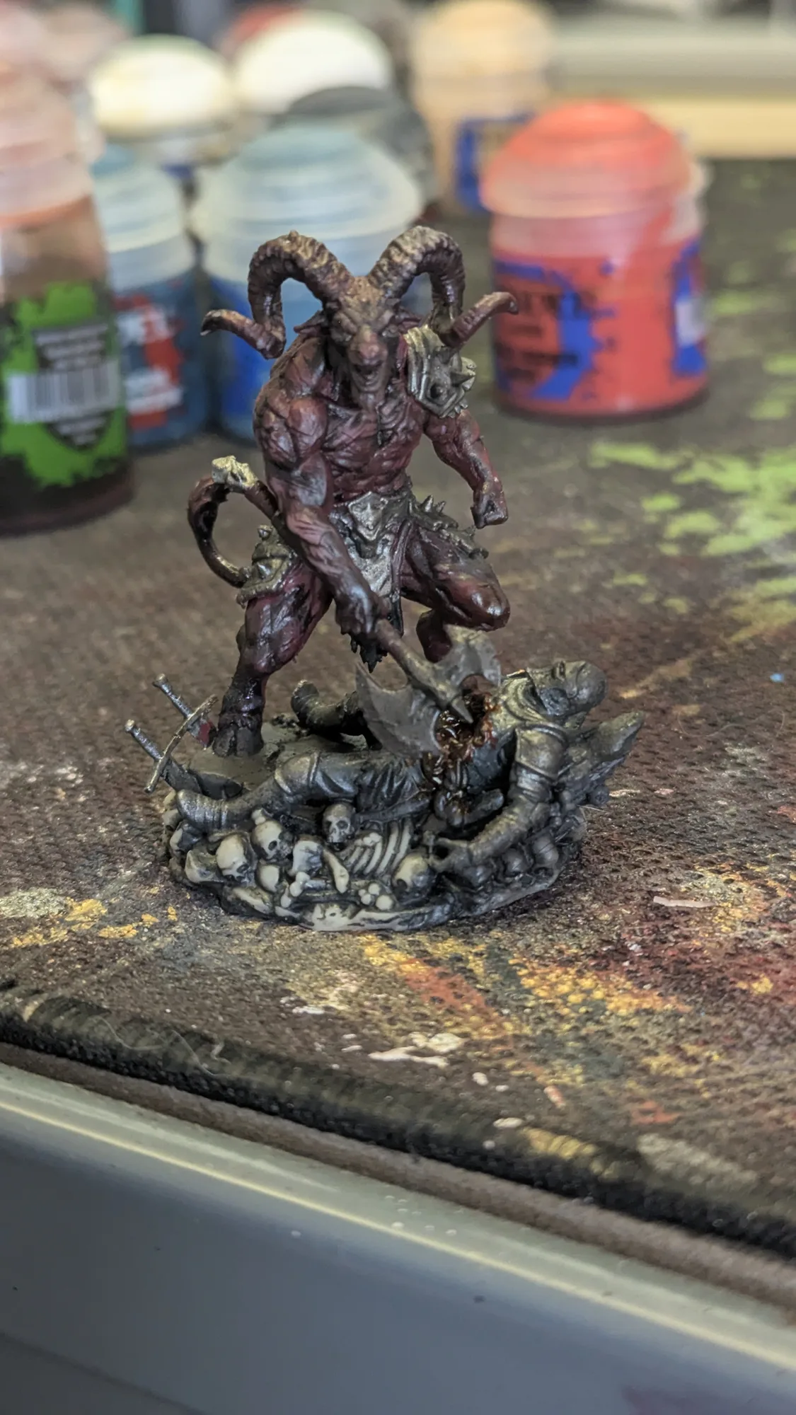 Figurine Demonlord Baalphagos de 55 mm imprimée en résine, démon cornu rouge sombre en cours de peinture sur le tapis de l'atelier