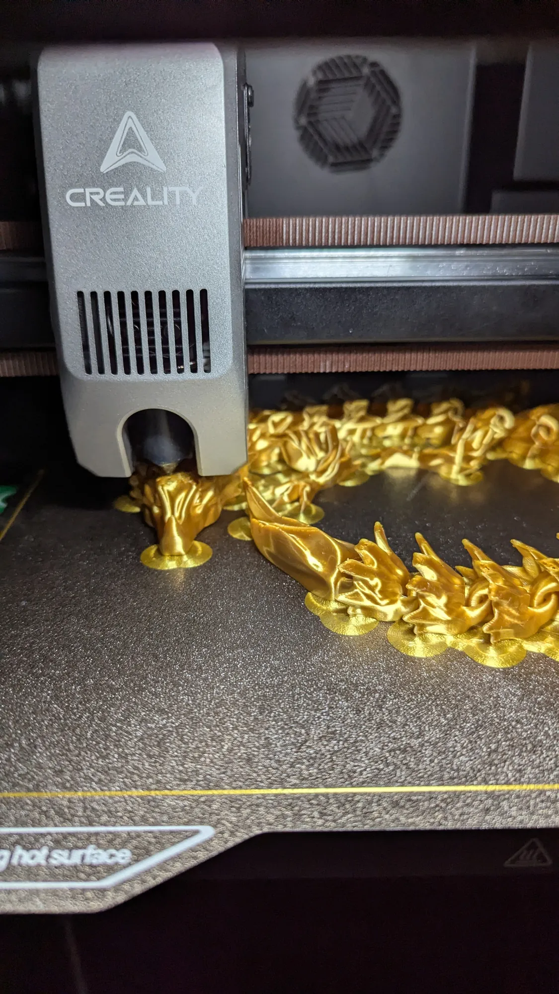 Dragon articulé doré imprimé en filament, encore sur le plateau de l'imprimante
